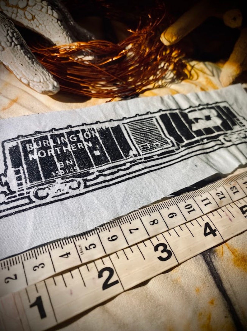 May include: Black and white image of a Burlington Northern train car with the number 23 on the side. The image is printed on a white fabric with a ruler measuring 13 inches.