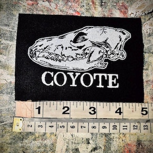 May include: Black fabric patch with a white outline of a coyote skull and the word "COYOTE" in white text.