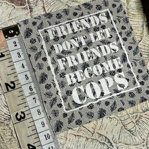 May include: A square fabric patch with a beige background and a black botanical leaf pattern. The text "FRIENDS DON'T LET FRIENDS BECOME COPS" is printed in white in the center. A measuring tape shows the patch is approximately 4 inches wide.