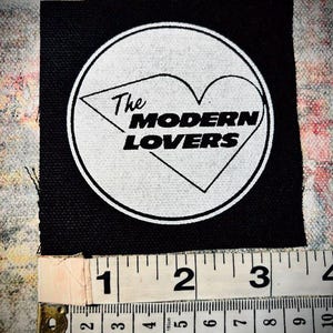 May include: A black fabric patch with a white circle containing a heart and the text "The Modern Lovers".