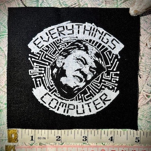 Op de afbeelding: Een zwart-witte strijkpatch met een witte cirkel met een gestileerde afbeelding van een gezicht met de tekst "EVERYTHINGS COMPUTER" rond de cirkel.