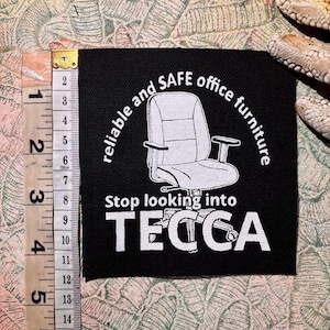 May include: Black square patch with white text and a drawing of an office chair. The text reads "reliable and SAFE office furniture" and "Stop looking into TECCA". A ruler shows the patch is approximately 2 inches wide.
