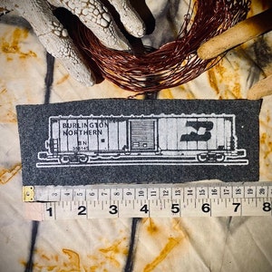 May include: A black and white illustration of a Burlington Northern train car with the number 3 on the side. The car is on a gray background and is about 8 inches long.