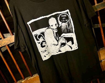 May include: Black t-shirt with a white graphic print of a person with a creepy smile and a speech bubble that says "Sounds gay, I'm in!"