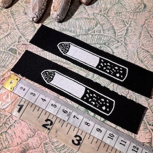 May include: Two black fabric patches with a white embroidered cigarette design. A ruler shows measurements in inches. The patches are approximately 6 inches long.