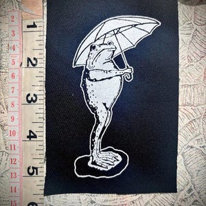 Trieste kikker die een paraplu vasthoudt naai op punkpatch