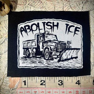 Puede incluir: Parche en blanco y negro con el texto "ABOLISH ICE" sobre una ilustración de un camión quitanieves. El parche mide aproximadamente 10 cm de ancho y 7,6 cm de alto.