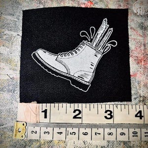 May include: Black and white illustration of a white boot with wooden sticks sticking out of the top. The boot is on a black background.