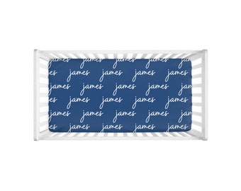 May include: A navy blue crib sheet with the name "James" repeated in white cursive writing.