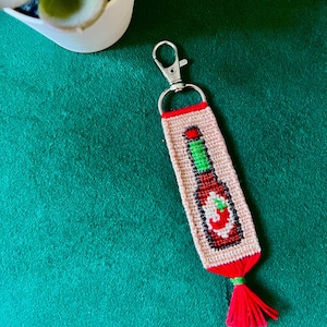 May include: A red and green embroidered keychain shaped like a bottle of ketchup with a red tassel.