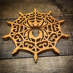 May include: A wooden wall hanging in the shape of a spider web with a spider in the center. The web is intricately carved with a detailed design.