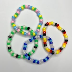 May include: Four colorful beaded bracelets, each with a different pattern of small, round beads. The bracelets are made with white, black, green, blue, yellow, orange, red, and pink beads.