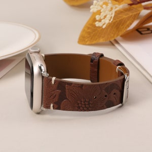 Puede incluir: Una correa de reloj de cuero marrón con un diseño floral en relieve. La correa es compatible con Apple Watch.