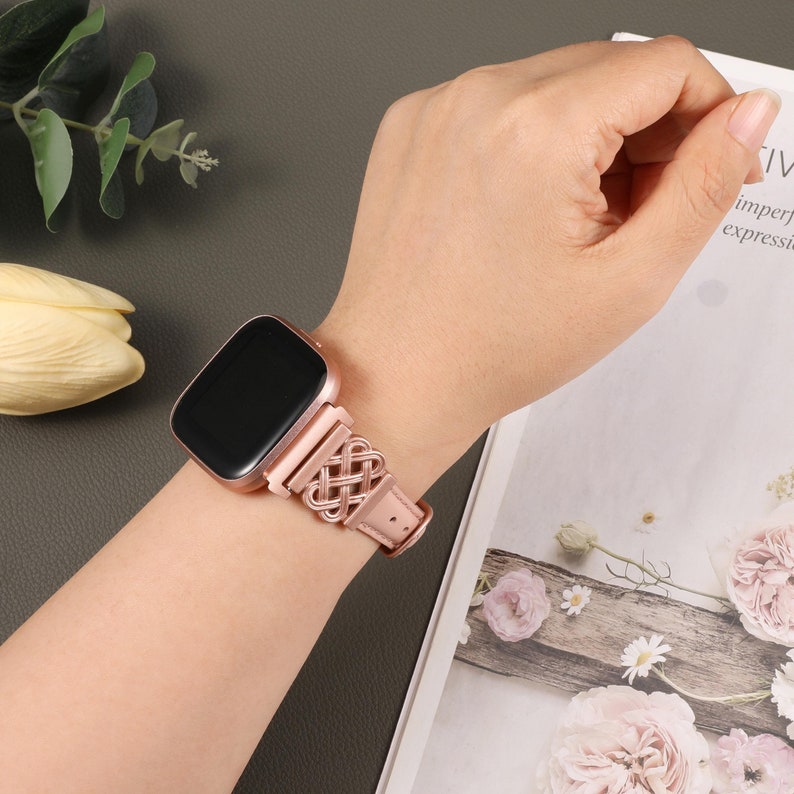 Puede incluir: Un smartwatch de color oro rosa con una banda trenzada de oro rosa. La esfera del reloj es negra y la banda es de cuero.