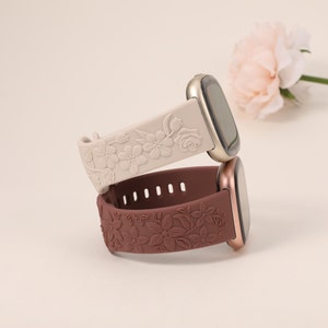 Puede incluir: Dos correas de reloj de silicona con diseños florales. La correa superior es blanca con un patrón floral y la correa inferior es marrón con un patrón floral.