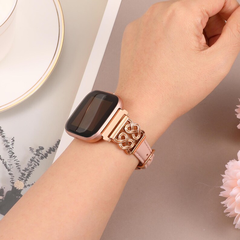 May include: A rose gold smartwatch with a rose gold metal band featuring a linked heart design. The band is attached to a square-shaped smartwatch with a black screen.