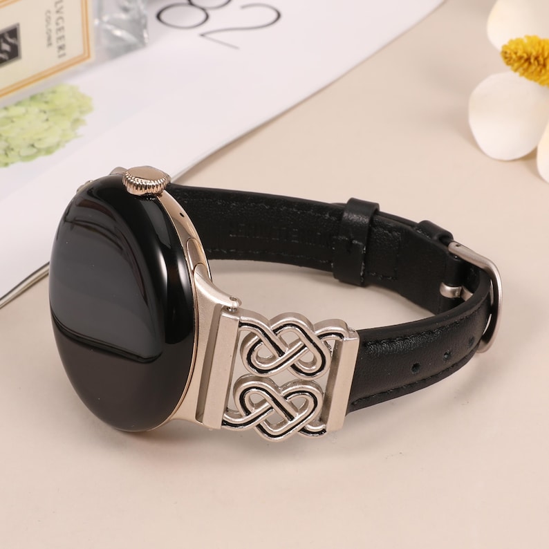 Pode incluir: Uma pulseira de rel&oacute;gio de couro preto com uma fivela de metal prateado com um design de n&oacute; intrincado. O mostrador do rel&oacute;gio &eacute; preto e redondo.