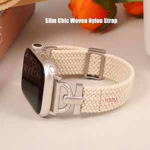 May include: A smartwatch with a cream-coloured woven nylon strap featuring a silver-toned metal connector and buckle. The strap width is marked as 16MM. The text Slim Chic Woven Nylon Strap is visible above the watch, which has a silver casing.