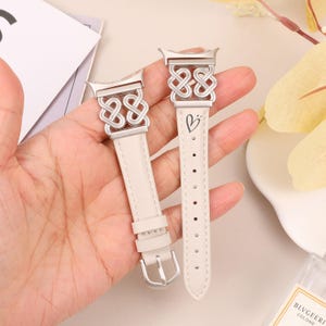 Pode incluir: Duas pulseiras de rel&oacute;gio de couro branco com fechos de metal prateado e um design de n&oacute; celta. O fecho de uma pulseira tem um s&iacute;mbolo de cora&ccedil;&atilde;o.