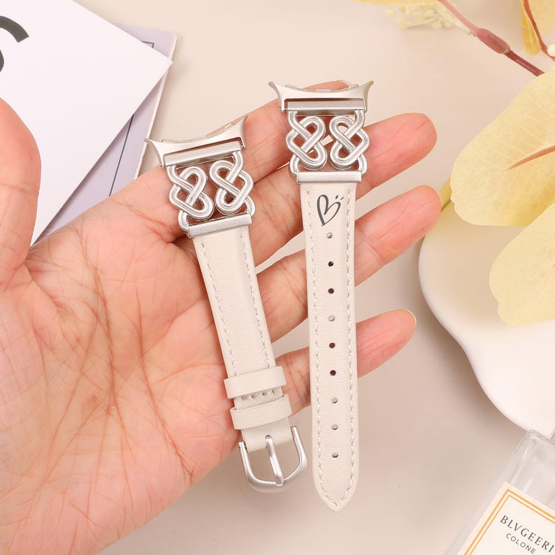 Pode incluir: Duas pulseiras de rel&oacute;gio de couro branco com fechos de metal prateado e um design de n&oacute; celta. O fecho de uma pulseira tem um s&iacute;mbolo de cora&ccedil;&atilde;o.