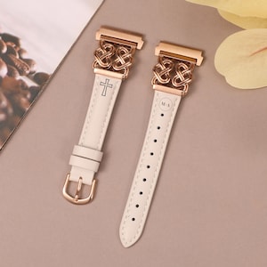 May include: Two white leather watch bands with rose gold metal clasps. One band has a cross design and the other has an interlocking circle design. Both bands have the letters "M-A" engraved on them.