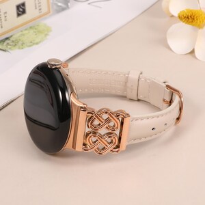 Pode incluir: Uma pulseira de rel&oacute;gio de couro branco com um fecho de metal dourado rosa com um design de n&oacute; intrincado. A pulseira &eacute; compat&iacute;vel com smartwatches.