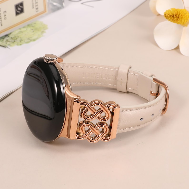 Pode incluir: Uma pulseira de rel&oacute;gio de couro branco com um fecho de metal dourado rosa com um design de n&oacute; intrincado. A pulseira &eacute; compat&iacute;vel com smartwatches.