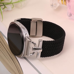 May include: A silver smartwatch with a black woven strap. The watch face is black and the strap has a metal clasp. The watch is designed for comfort and style.