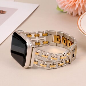 May include: A silver and gold metal watch band with a square link design. The band is compatible with Apple Watch.