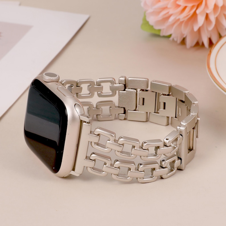May include: A silver metal watch band with a chain link design. The band is compatible with Apple Watch.