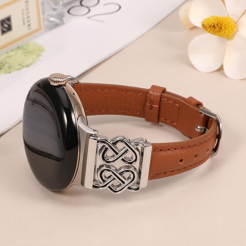 Pode incluir: Uma pulseira de rel&oacute;gio de couro marrom com uma fivela de metal prateado com um design de n&oacute; intrincado. A pulseira &eacute; compat&iacute;vel com smartwatches.
