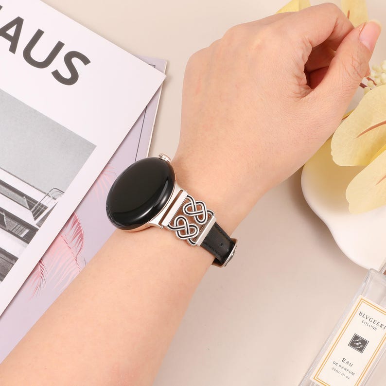 Pode incluir: Um smartwatch preto com uma banda de metal prateada com um design de n&oacute; celta. A banda &eacute; de couro preto com uma faixa branca.