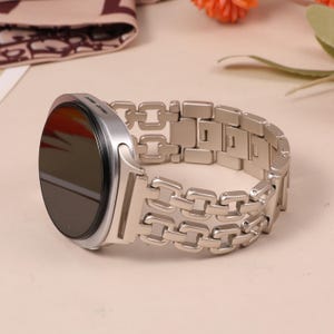 May include: A silver smartwatch with a black screen and a matching stainless steel chain-link band. The watch is round with a sleek, modern design. The band features a series of interconnected rectangular links.