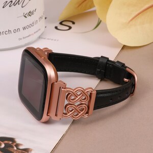 May include: A rose gold smartwatch with a black leather band and a decorative rose gold clasp. The band has a double infinity symbol design.