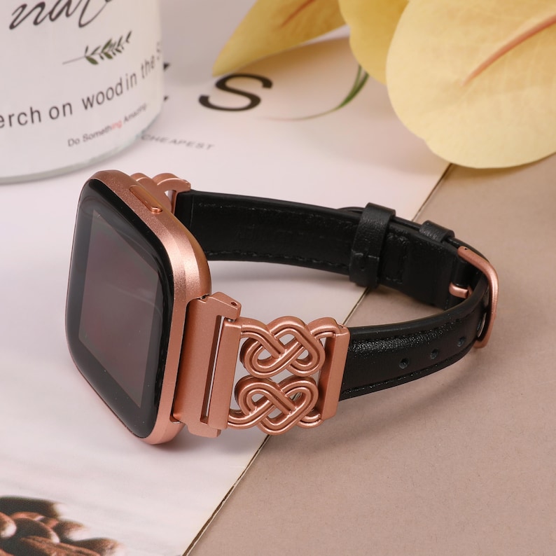 May include: A rose gold smartwatch with a black leather band and a decorative rose gold clasp. The band has a double infinity symbol design.