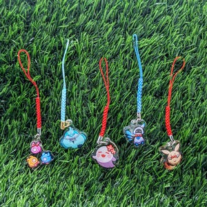 May include: Five colorful keychains with different cartoon characters. The keychains are made of clear plastic and have red, blue, and white strings.