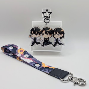 May include: A clear acrylic keychain featuring three anime characters with black hair. The characters are wearing white lab coats and are holding a phone, a black bag, and a phone. The keychain is attached to a black and white lanyard with a silver clip.