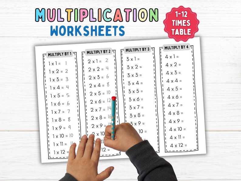 May include: A set of four black and white multiplication worksheets for learning the 1-12 times tables. The worksheets are labeled "Multiply by 1", "Multiply by 2", "Multiply by 3", and "Multiply by 4". A child's hand is holding a blue pen and writing on the worksheet.