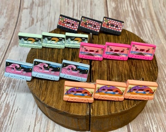 May include: A set of eight colorful cassette tape earrings with various designs, including palm trees, waves, and a starry sky. The earrings are made of polymer clay and are perfect for adding a touch of retro style to any outfit.