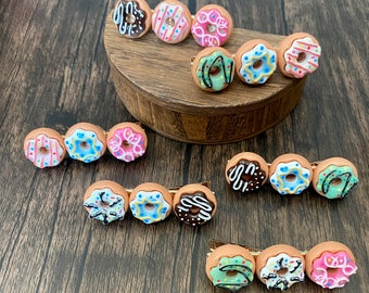 May include: A set of 10 donut-shaped hair clips in various colors, including pink, blue, brown, and white. The clips are decorated with sprinkles and icing.