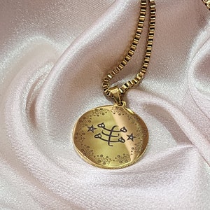 May include: A gold chain necklace with a round pendant featuring a black symbol and floral design. The pendant is surrounded by five stars.