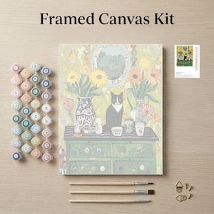 The image is a framed canvas kit featuring a painting of a cat sitting on a table surrounded by various objects, such as vases, cups, and a clock. The kit also includes paintbrushes, paint tubes, and a small picture frame.