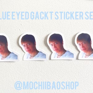 May include: A sticker set featuring four stickers with a portrait of a person with short brown hair, blue eyes, and a gold necklace. The text "BLUE EYED GACKT STICKER SET!" is above the stickers, and the shop's name is below.