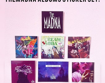 May include: A set of square stickers featuring album art designs. The stickers showcase various colorful illustrations and text, including "THE MADNA" and album titles like "Ugly Heaven" and "Cream Soda." The stickers are arranged on a pink background.