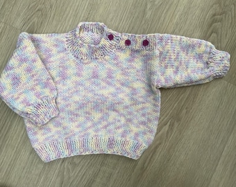 May include: A hand-knitted baby sweater in a soft, pastel color palette of lavender, white, and pale yellow. The sweater features a round neckline, long sleeves, and three purple buttons on the shoulder. The knitwear is a cozy, handmade item.