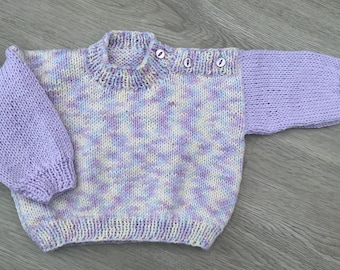 May include: A purple and white knit baby sweater with a contrasting solid purple sleeve. The sweater has a round neck and three buttons on the shoulder.
