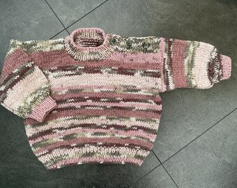 May include: A striped knitted sweater in shades of pink, brown, and white. The sweater has a round neckline and long sleeves.