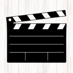 May include: A black film clapperboard with white detailing against a light wood grain backdrop. The clapperboard, a traditional filmmaking tool, has a hinged top section with alternating black and white stripes.
