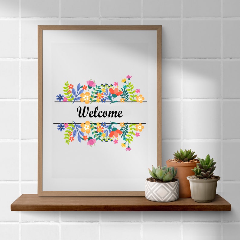 May include: A framed print with a floral design and the word "Welcome" in black text. The print is on a shelf with three potted succulents.