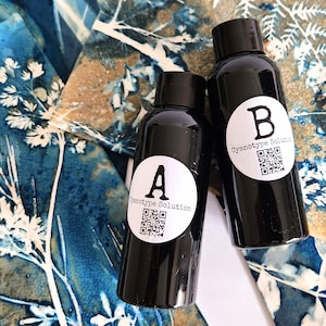 K&ouml;nnte beinhalten: Zwei schwarze Flaschen mit wei&szlig;en Etiketten. Die Etiketten haben einen Kreis mit dem Buchstaben A oder B darin und den Text "Cyanotype Solution".